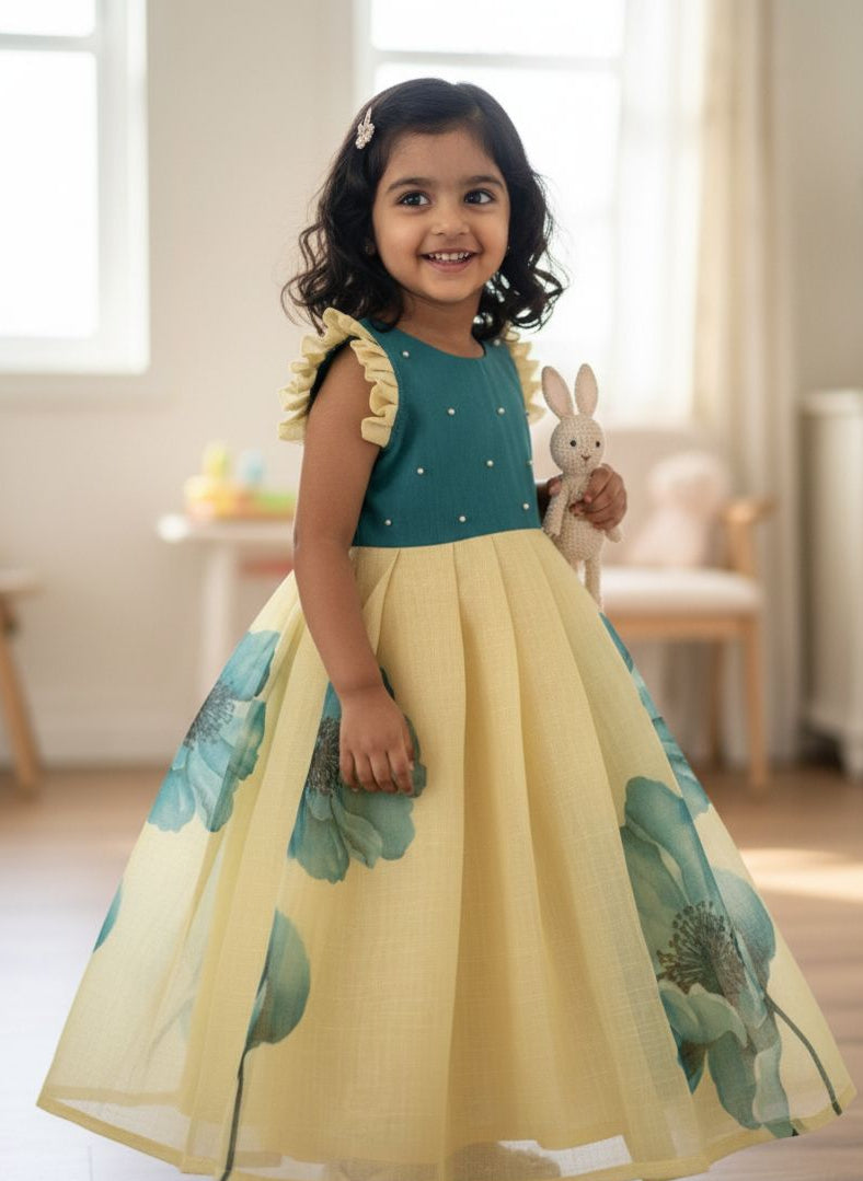 Young girl in a yellow dress with green floral patterns, holding a stuffed rabbit toy, standing in a bright room.